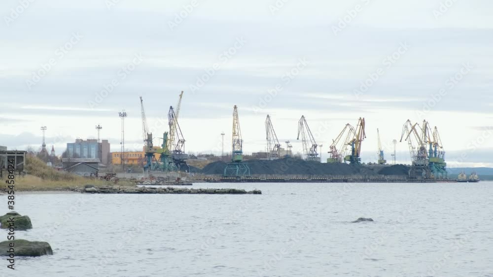 Port Cranes During Operation. The port marine crane unloads coal from railway cars to a dry cargo ship in the background of the gulf Port Cranes During Operation. The port marine crane unloads coal from railway cars to a dry cargo ship in the background of the gulf