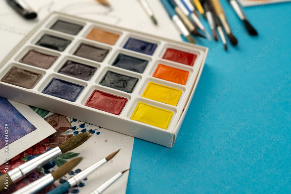 Watercolor paints and brushes. Artist's workplace and desk. Color palette. Drawing blue background. Place for your text. Art created. Copy space.