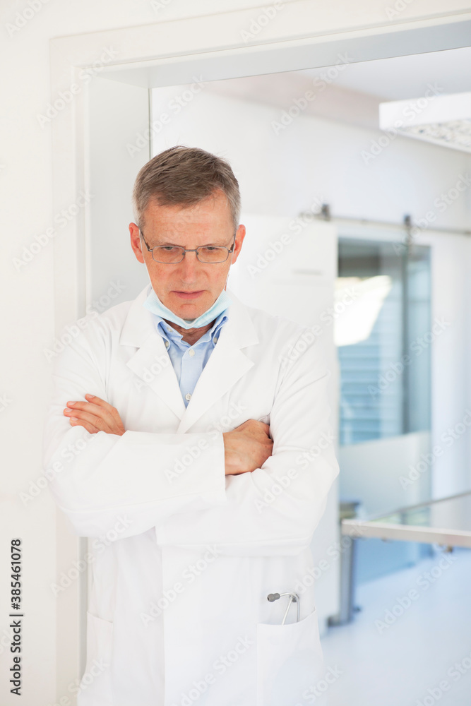 Tired and sad mature doctor standing in front of his surgery