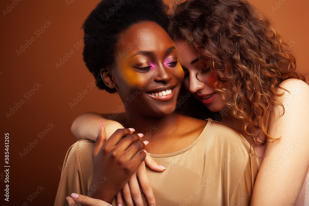Obraz premium two pretty girls african and caucasian blond posing cheerful together on brown background, ethnicity diverse lifestyle people concept