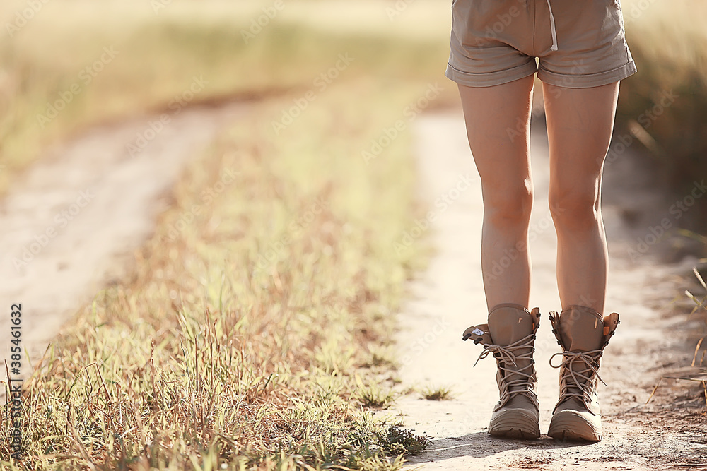 female legs in summer trekking boots / walks anonymously on the field woman big shoes girl