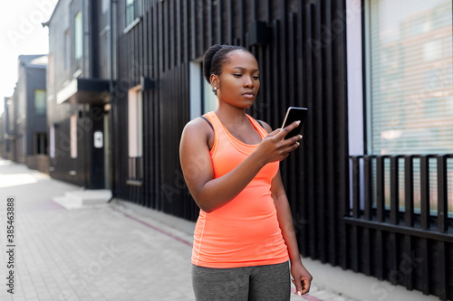 fitness, sport and technology concept - young african american woman with smartphone exercising in city