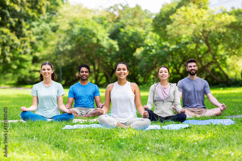fitness, sport, yoga and healthy lifestyle concept - group of happy people meditating in lotus pose at summer park