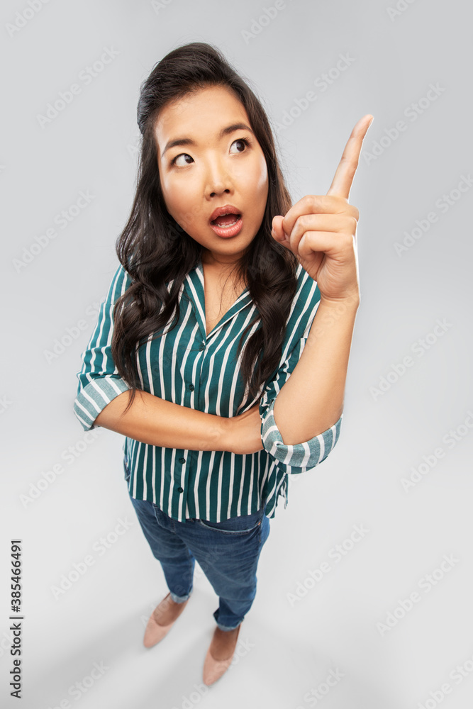 people, idea and emotions concept - asian young woman pointing finger up over grey background people, idea and emotions concept - asian young woman pointing finger up over grey background