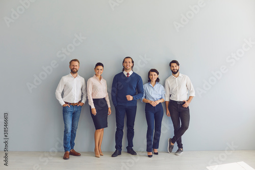 Group portrait of happy businesspeople standing near office wall looking at camera