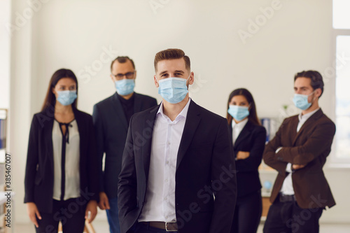 Portrait of business owner with team of employees all wearing face masks in office after reopening