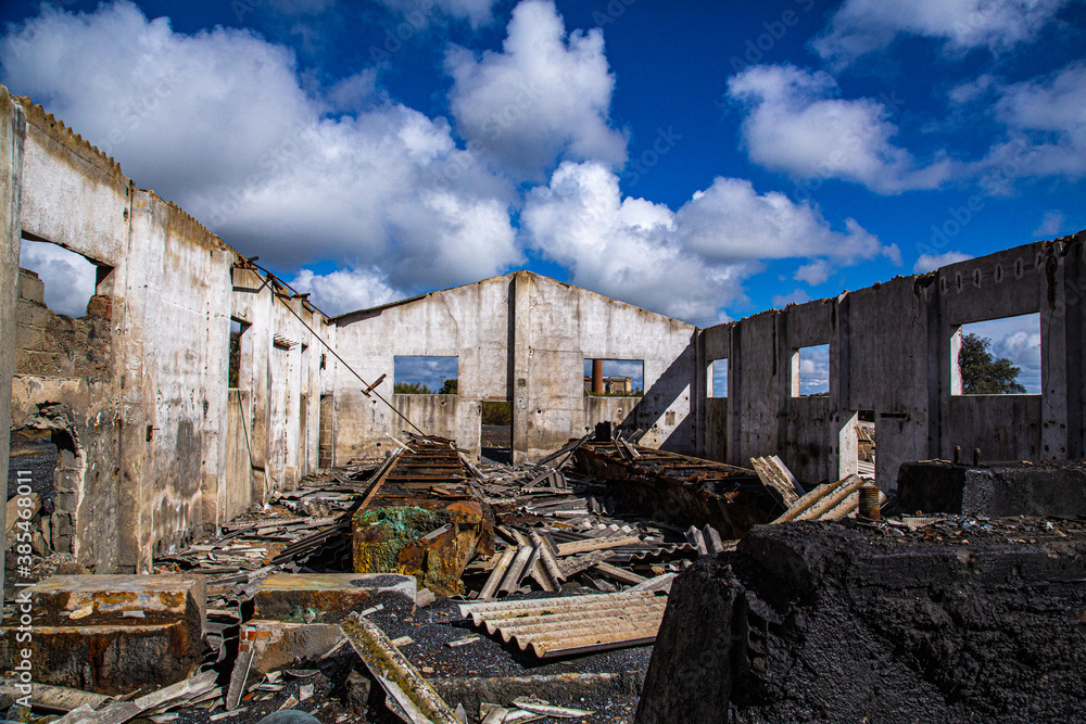 Fototapeta premium Interior de almacén industrial con tejado derruido y cielo lleno de nubes