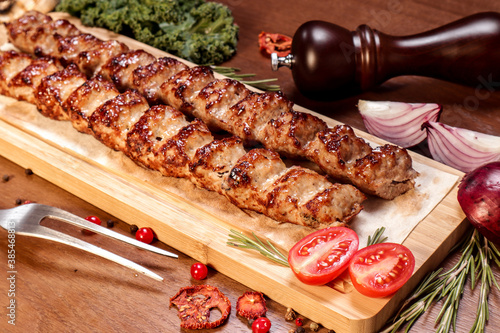 Lula kebab fried on charcoal with vegetables and spices on a wooden board.