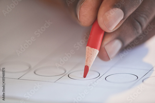 Close-up of man putting the tick on ballot with red pencil during voting