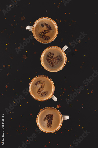 New year 2021 numbers on foamed coffee cups written from cocoa powder on black background among golden stars.