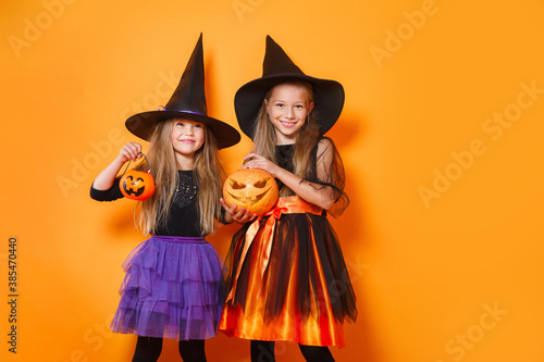 Two little girls in halloween costumes having fun on orange studio background