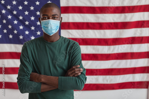 Portrait of Afro-American man in protective mask standing with his arms crossed and looking at camera against the American flag photo