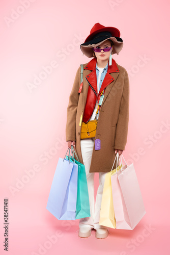 woman in sunglasses and hats with sale tags holding shopping bags and standing on pink