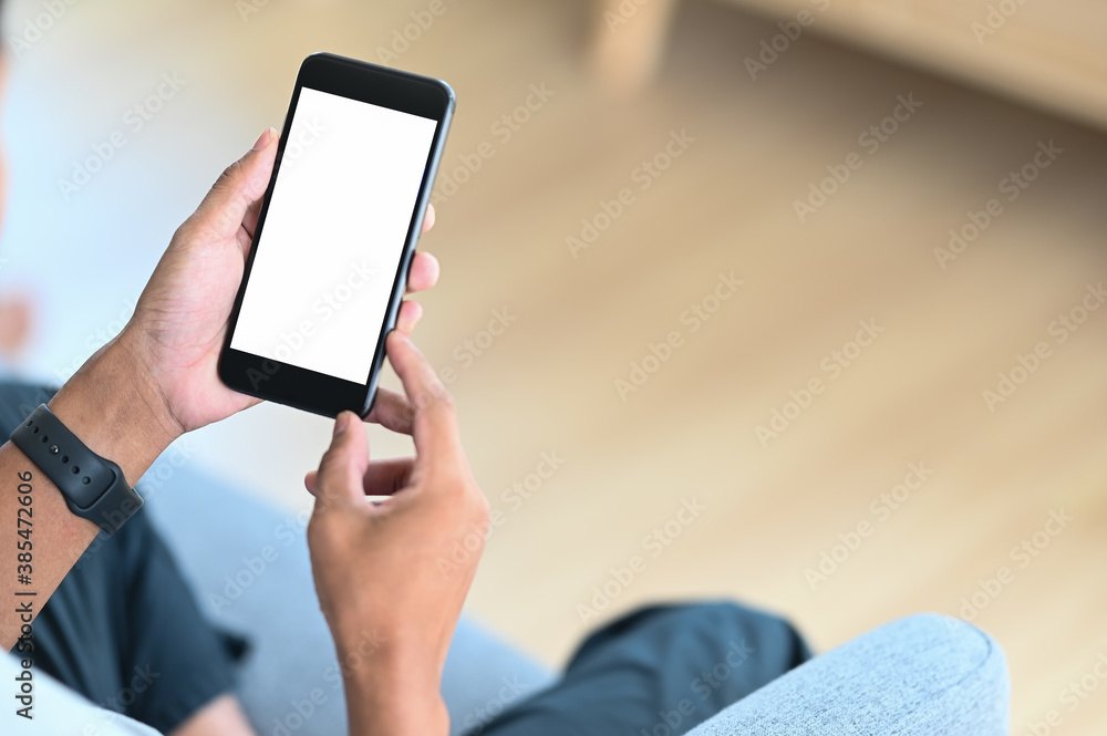 Cropped image of man using mobile phone with empty screen in hands on couch. Cropped image of man using mobile phone with empty screen in hands on couch.