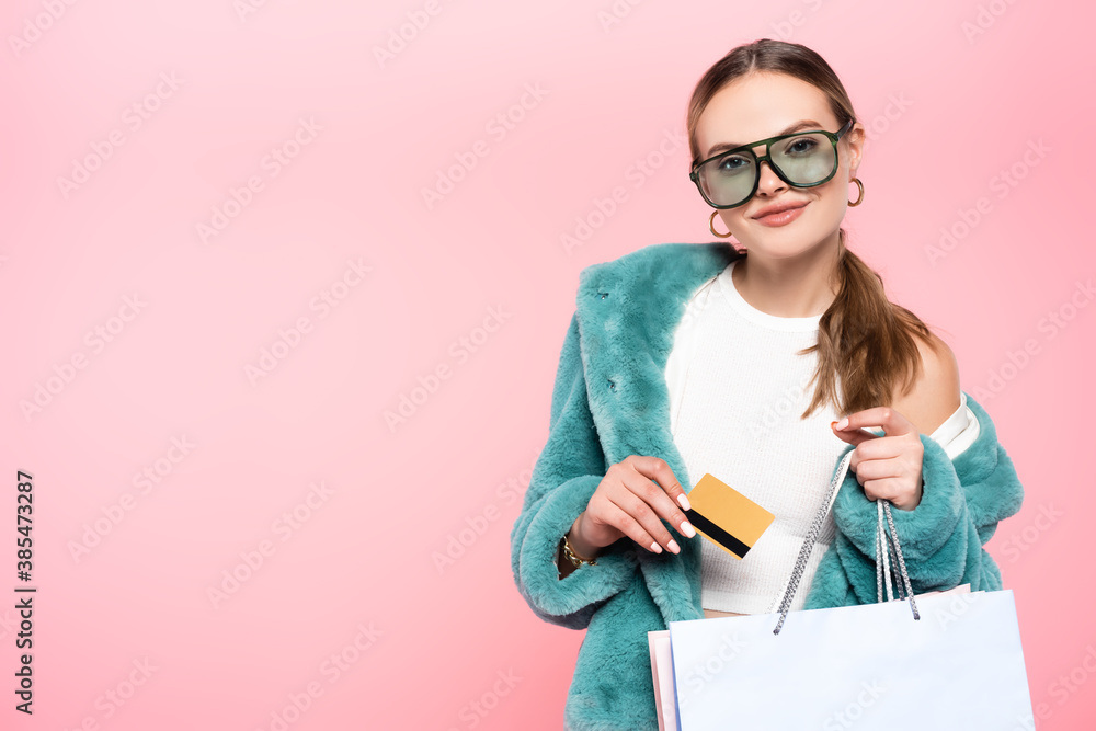 trendy woman in sunglasses holding credit card near shopping bag isolated on pink, black friday concept trendy woman in sunglasses holding credit card near shopping bag isolated on pink, black friday concept