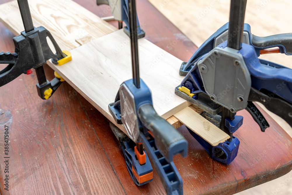 Joining wooden handmade box with clamps joiners after glueing. Different chisels, drills and pencils at craftsman workshop. DIY instruments on wood workbench. Workplace organization arrangement Joining wooden handmade box with clamps joiners after glueing. Different chisels, drills and pencils at craftsman workshop. DIY instruments on wood workbench. Workplace organization arrangement