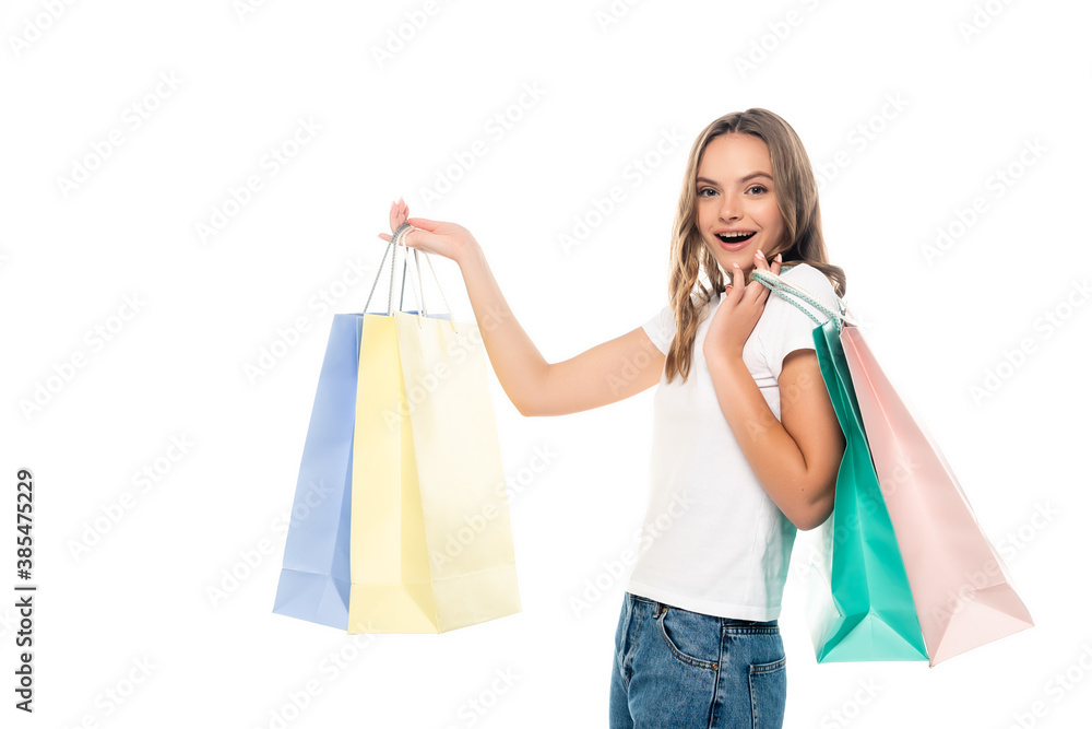 young excited woman holding colorful shopping bags and looking at camera isolated on white