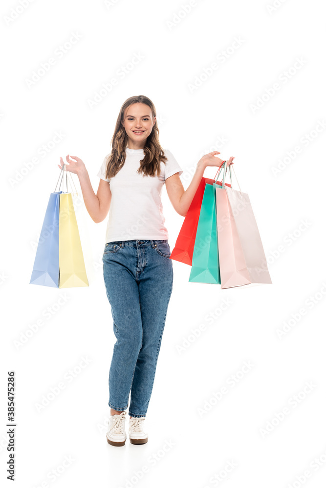 joyful young woman holding colorful shopping bags and looking at camera isolated on white