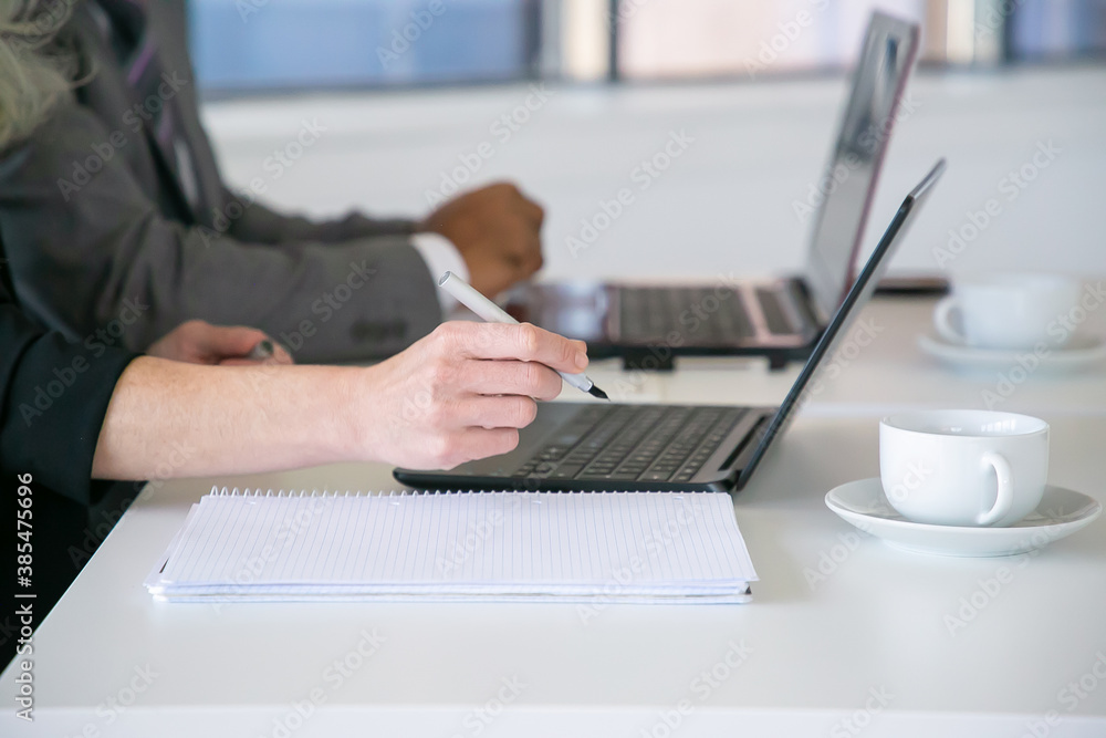 Office workers writing notes, using laptop at table with cups of coffee. Closeup of hands, cropped shot. Education or digital communication concept Office workers writing notes, using laptop at table with cups of coffee. Closeup of hands, cropped shot. Education or digital communication concept