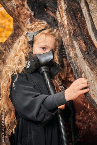 portrait of a little girl in a mask with a respirator against the background of a textured destroyed large tree. concept ecology pandemic salvation