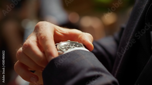 Unrecognizable man looking at wrist watch in park. Guy hiding watch under sleeve