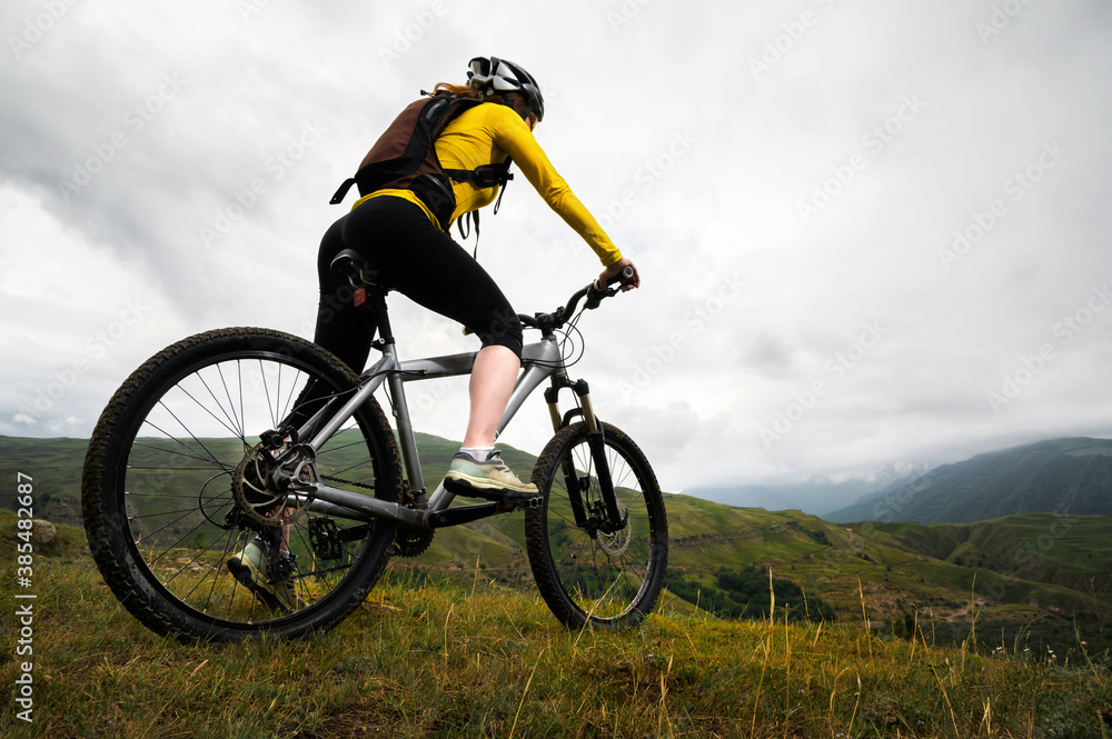 Wide angle. Young woman in a helmet and with a backpack stands with a bicycle mountains in cloudy weather. Mountain mtb bike