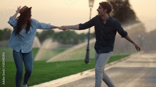 Strong man taking woman on hands on road. Girl and guy spinning around in park