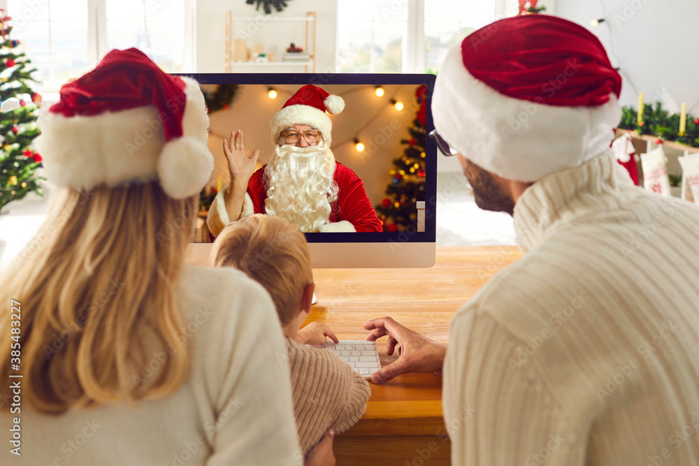 Mom, dad and kid looking at computer screen while having video call with Santa Claus - obrazy, fototapety, plakaty 