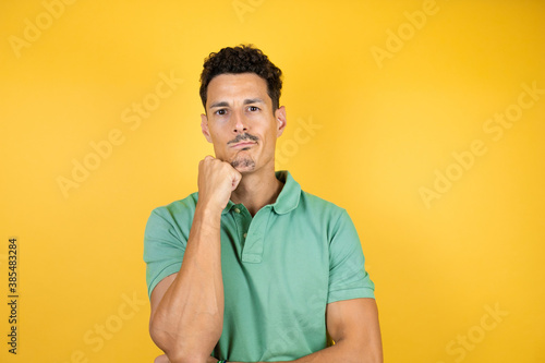 Young handsome man wearing green casual t-shirt over isolated yellow background thinking looking tired and bored with crossed arms