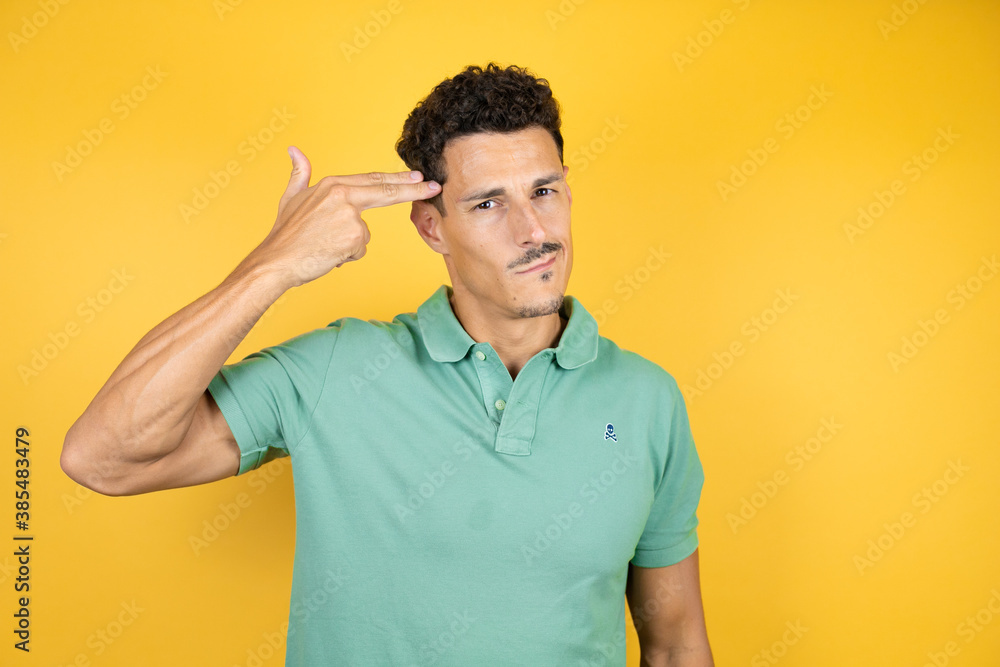 Young handsome man wearing green casual t-shirt over isolated yellow background Shooting and killing oneself pointing hand and fingers to head like gun, suicide gesture. Young handsome man wearing green casual t-shirt over isolated yellow background Shooting and killing oneself pointing hand and fingers to head like gun, suicide gesture.