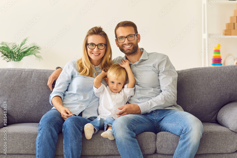 Happy mom, dad and son sitting on comfy couch in living room while spending time together at home