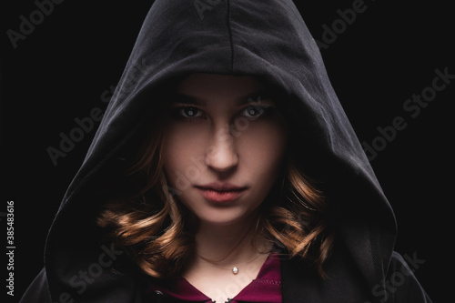 Close-up portrait of a secretive young girl in a deep dark hood on a black background. The concept of secrecy of secrets and people hiding from the government.