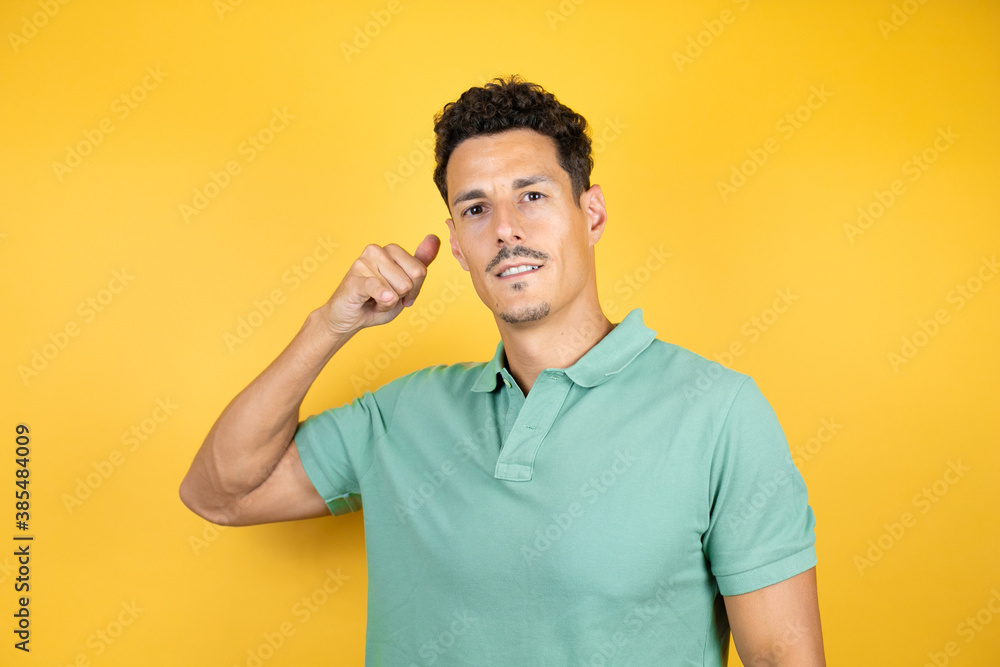 Young handsome man wearing green casual t-shirt over isolated yellow background smiling doing phone gesture with hand and fingers like talking on the telephone Young handsome man wearing green casual t-shirt over isolated yellow background smiling doing phone gesture with hand and fingers like talking on the telephone
