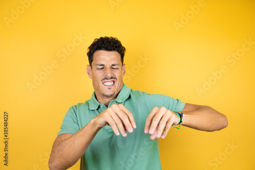 Young handsome man wearing green casual t-shirt over isolated yellow background disgusted expression, displeased and fearful doing disgust face because aversion reaction. Annoying concept