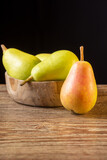 Close-up of several ercolinas pears in wooden bowl, on wooden table and black background in vertical, with copy space
