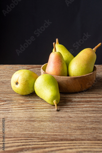 Top view of several ercolinas pears in wooden bowl, on wooden table and black background in vertical, with copy space