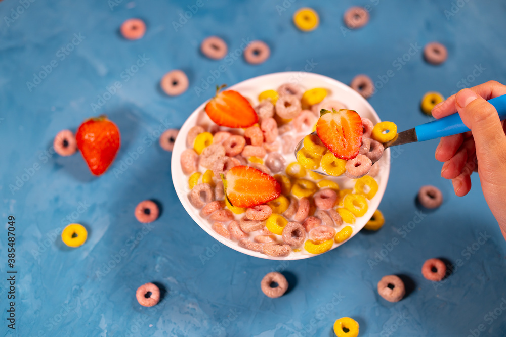 Healthy breakfast with cereal and berries. From above of bowl with delicious healthy breakfast made with colorful cereal rings and fresh strawberry with milk served on blue table Healthy breakfast with cereal and berries. From above of bowl with delicious healthy breakfast made with colorful cereal rings and fresh strawberry with milk served on blue table