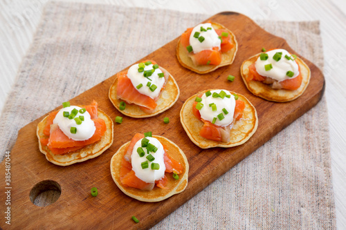 Foto Homemade Blini with Smoked Salmon, Creme and Chives on a rustic wooden board, side view