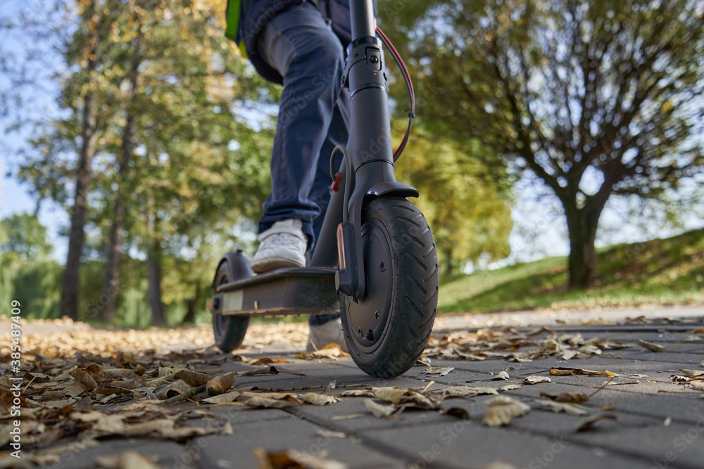 Obraz premium The boy is riding on the electric scooter through the park