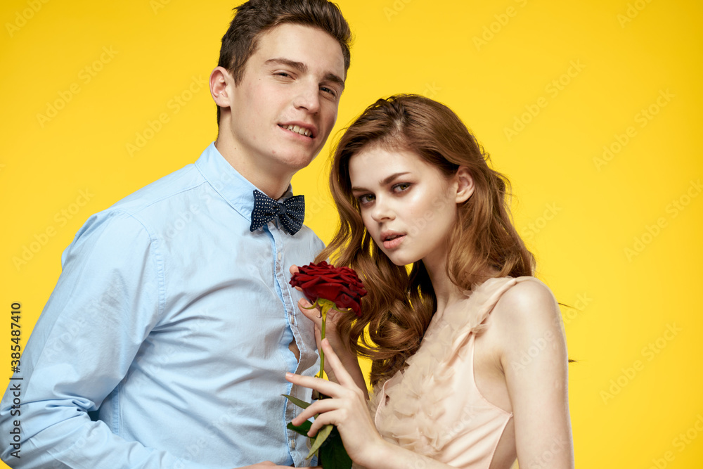 A loving young couple with a red rose in their hands are hugging on a yellow background A loving young couple with a red rose in their hands are hugging on a yellow background
