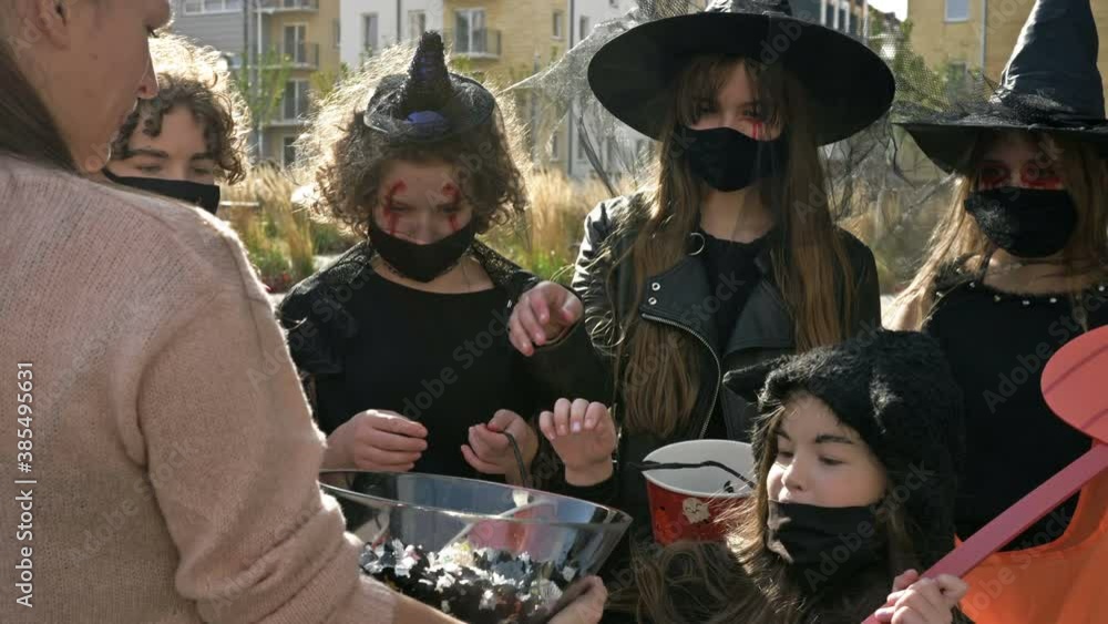 Woman treats sweets to a group of children in black fancy dress with scary makeup on their faces. Halloween traditions. Woman treats sweets to a group of children in black fancy dress with scary makeup on their faces. Halloween traditions.