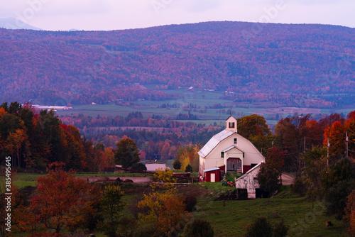 vintage white barn in the valley of vibrant hills and mountains during fall changing colors in new hampshire USA 