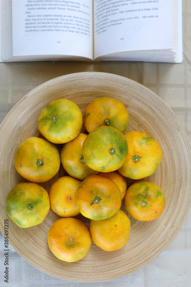 Bowl of tangerines and open book on a table. Top view. 