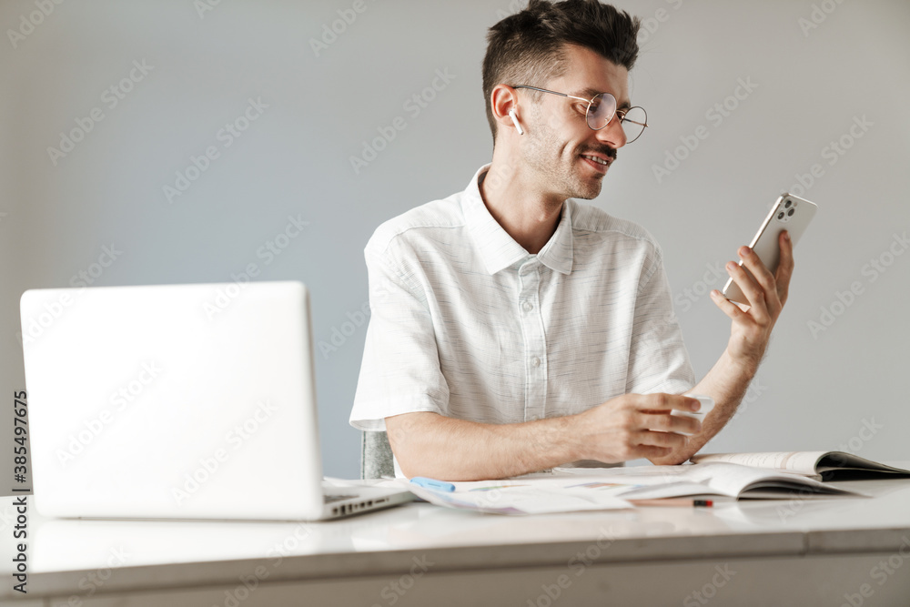 Photo of smiling man using earphones and cellphone working with laptop Photo of smiling man using earphones and cellphone working with laptop