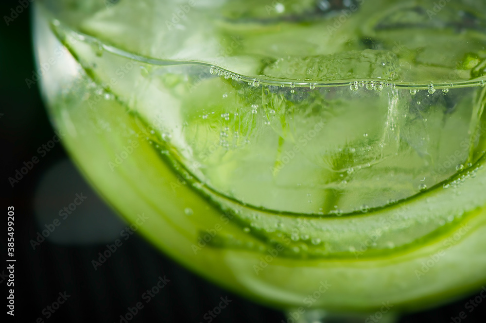 Green fresh cucumber drink closeup with small bubbles and ice cubes in a round glass Green fresh cucumber drink closeup with small bubbles and ice cubes in a round glass