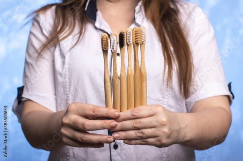 a lot of bamboo toothbrushes in female hands close-up. girl with a smile out of focus. ecologicaly clean. biodegradable hygiene items. multi-colored bristles. place for text.  photo