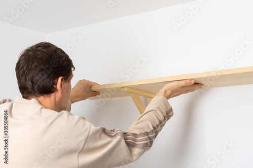 Bild auf Leinwand A man hangs a shelf in an apartment on a white wall, a worker checks the evennes