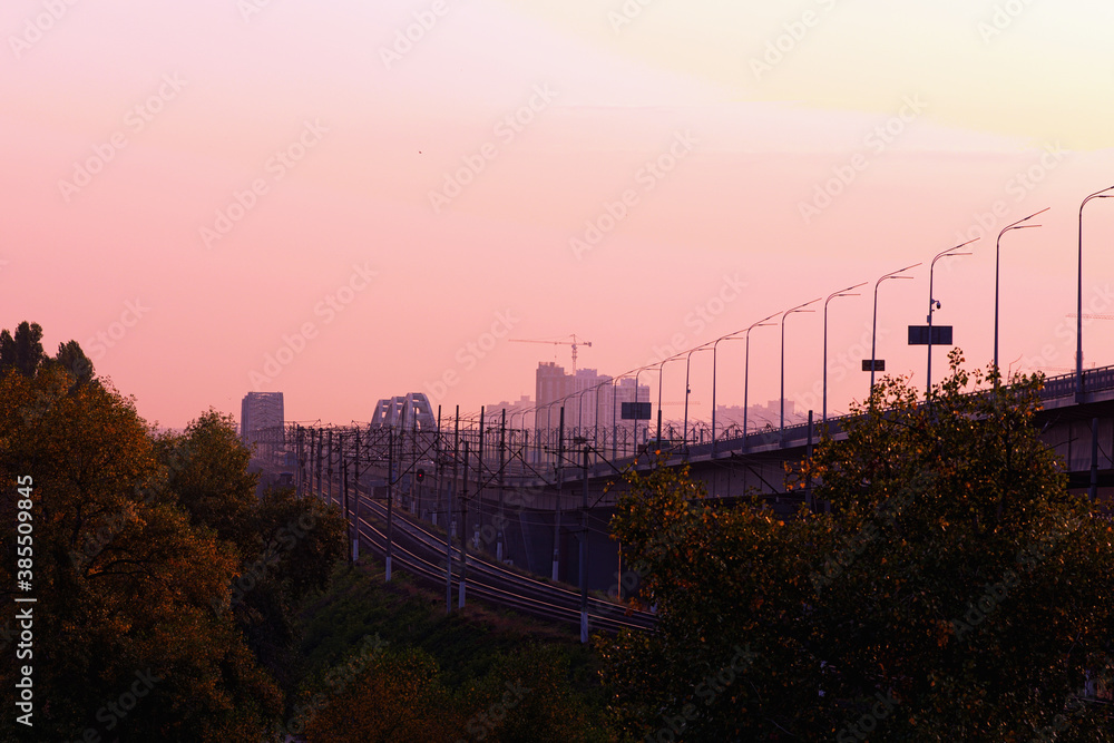 Obraz premium The New Darnytskyi Bridge is a combined road and railroad bridge in Kyiv over Dnipro River. Majestic morning landscape view of railroad bridge and road bridge with vehicles.Scenic autumn morning view.