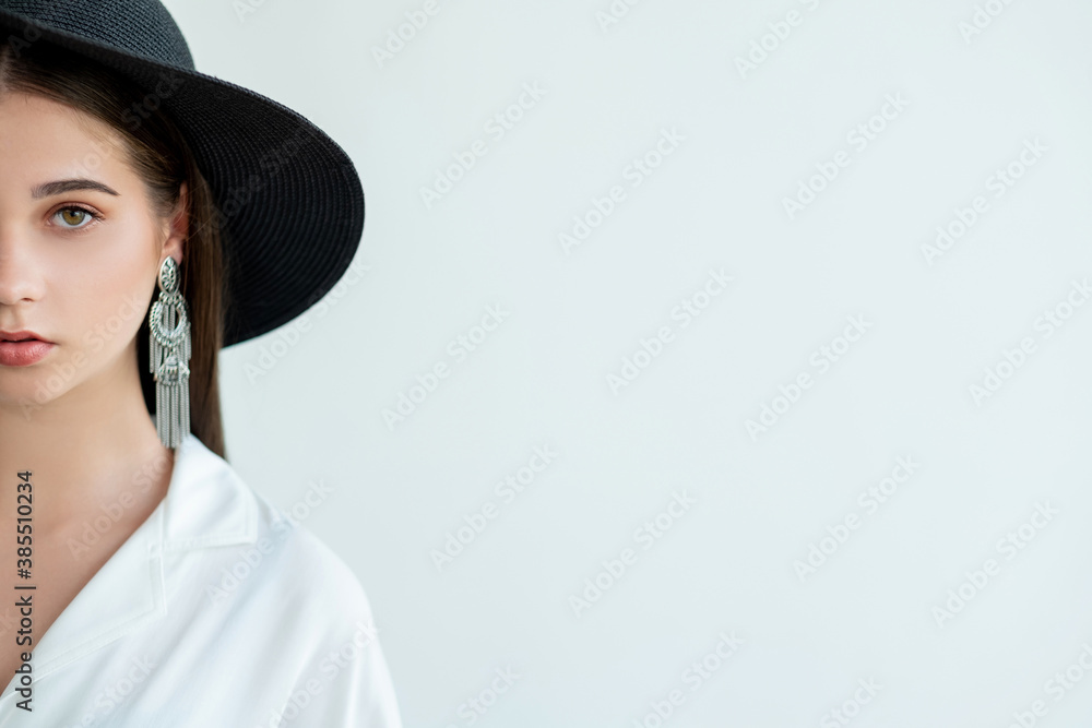 Trend fashion. Casual outfit. Elegant young woman in wide-brimmed black hat vintage earrings white blouse looking at camera half face isolated on neutral copy space. Summer look. Model shooting Trend fashion. Casual outfit. Elegant young woman in wide-brimmed black hat vintage earrings white blouse looking at camera half face isolated on neutral copy space. Summer look. Model shooting