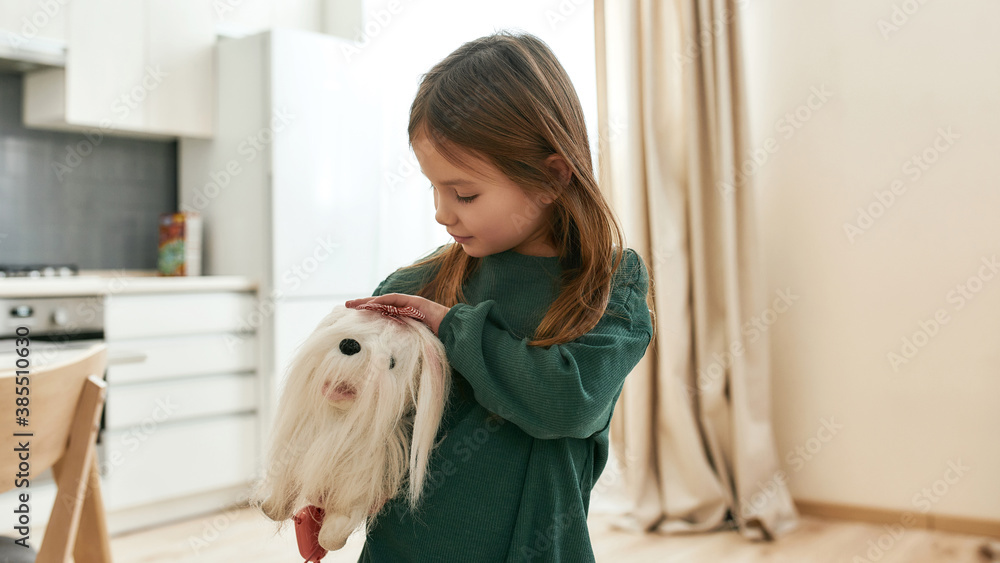 A cute small girl holding and pesting her toy dog under her arm A cute small girl holding and pesting her toy dog under her arm